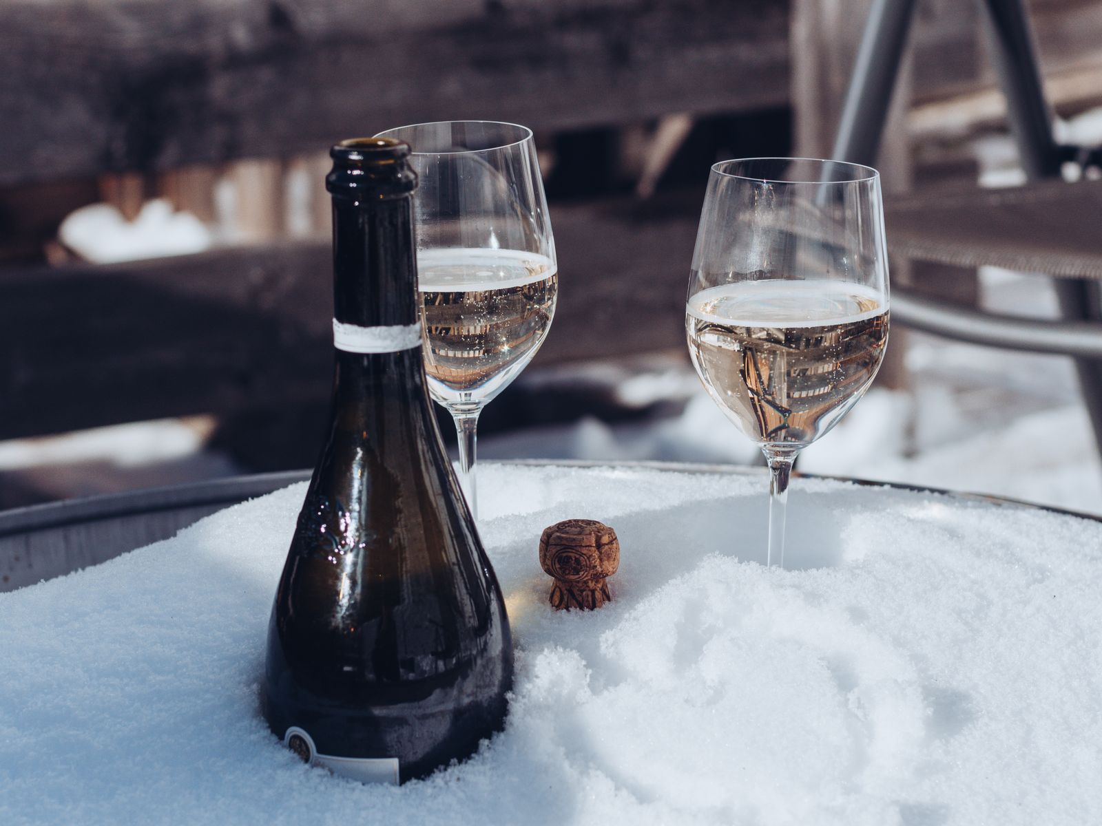 A bottle of champagne and two glasses resting in the snow