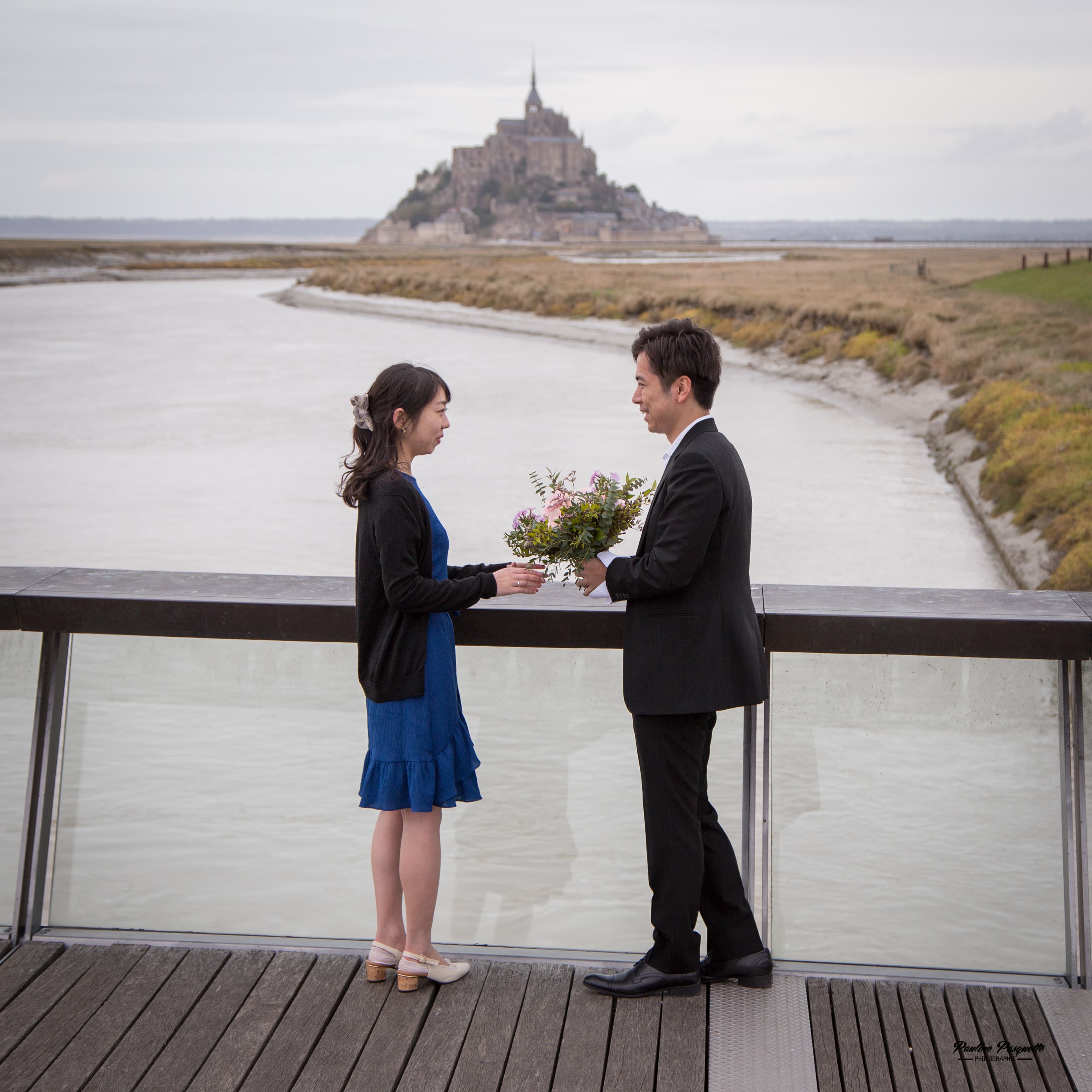 A couple at the moment of their proposal, the abbey of Mont-Saint-Michel rising behind them