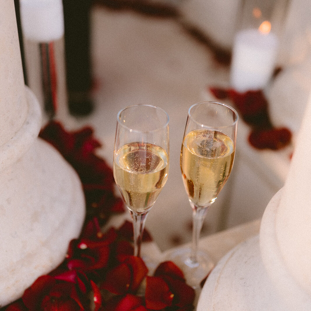 Two champagne flutes among rose petals and candlelight