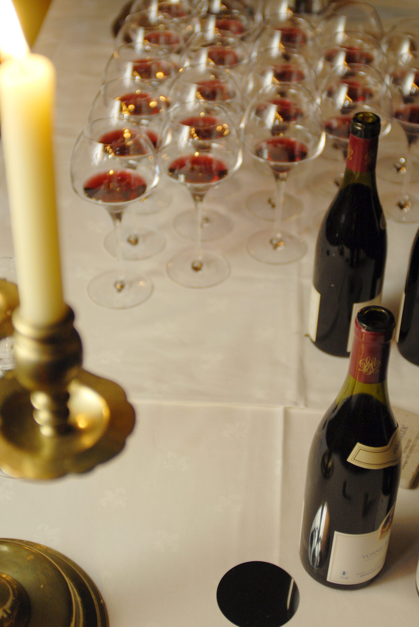 A candle, poured glasses and an old bottle on a white cloth
