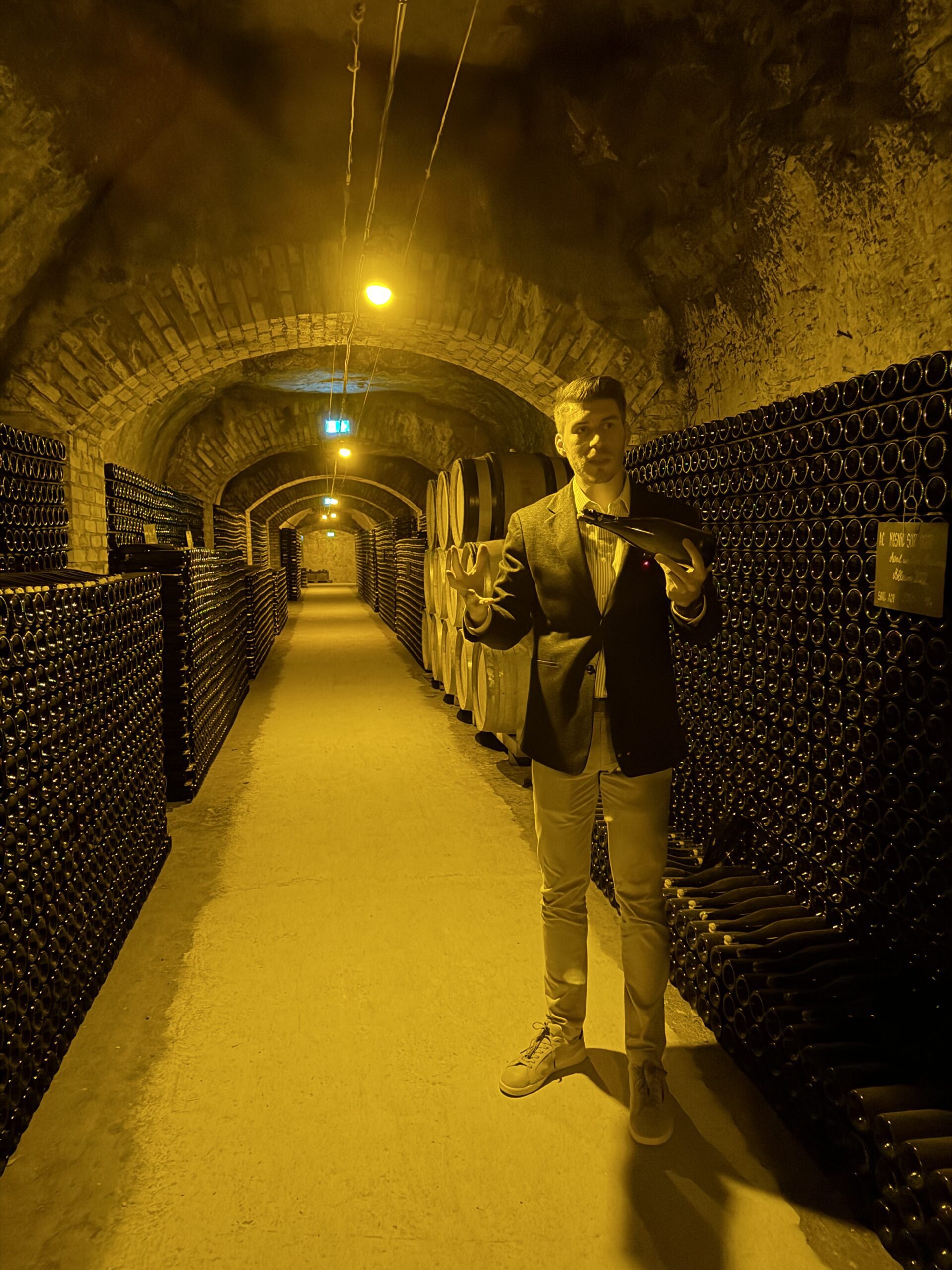 Beneath Europe: Roman Cellars, Cave Cities and a Lake in the Dark 2 A host presenting a bottle in a Champagne cellar gallery lined with ageing bottles